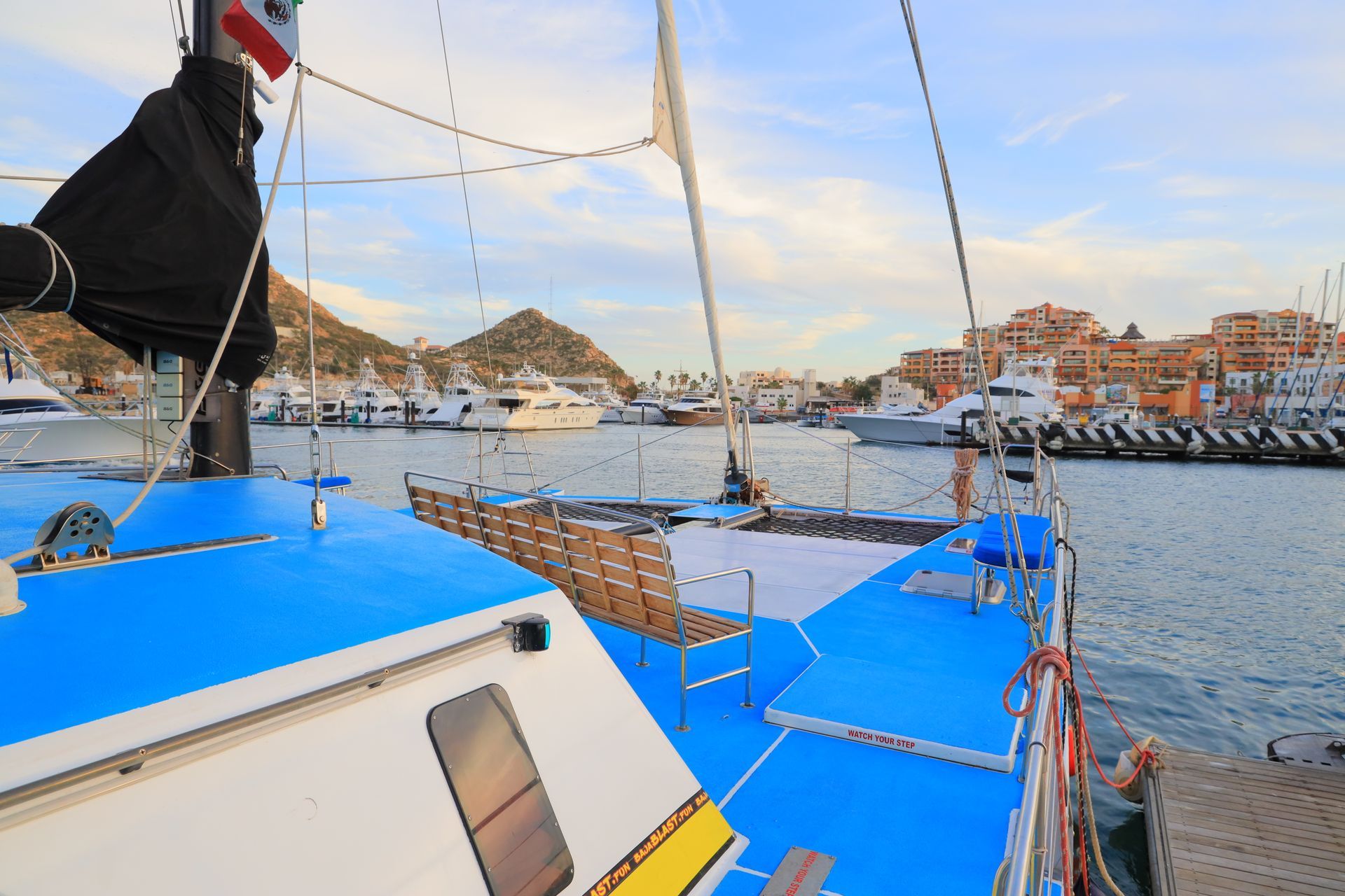 Blue sailboat deck in a harbor with moored boats and waterfront buildings at sunset