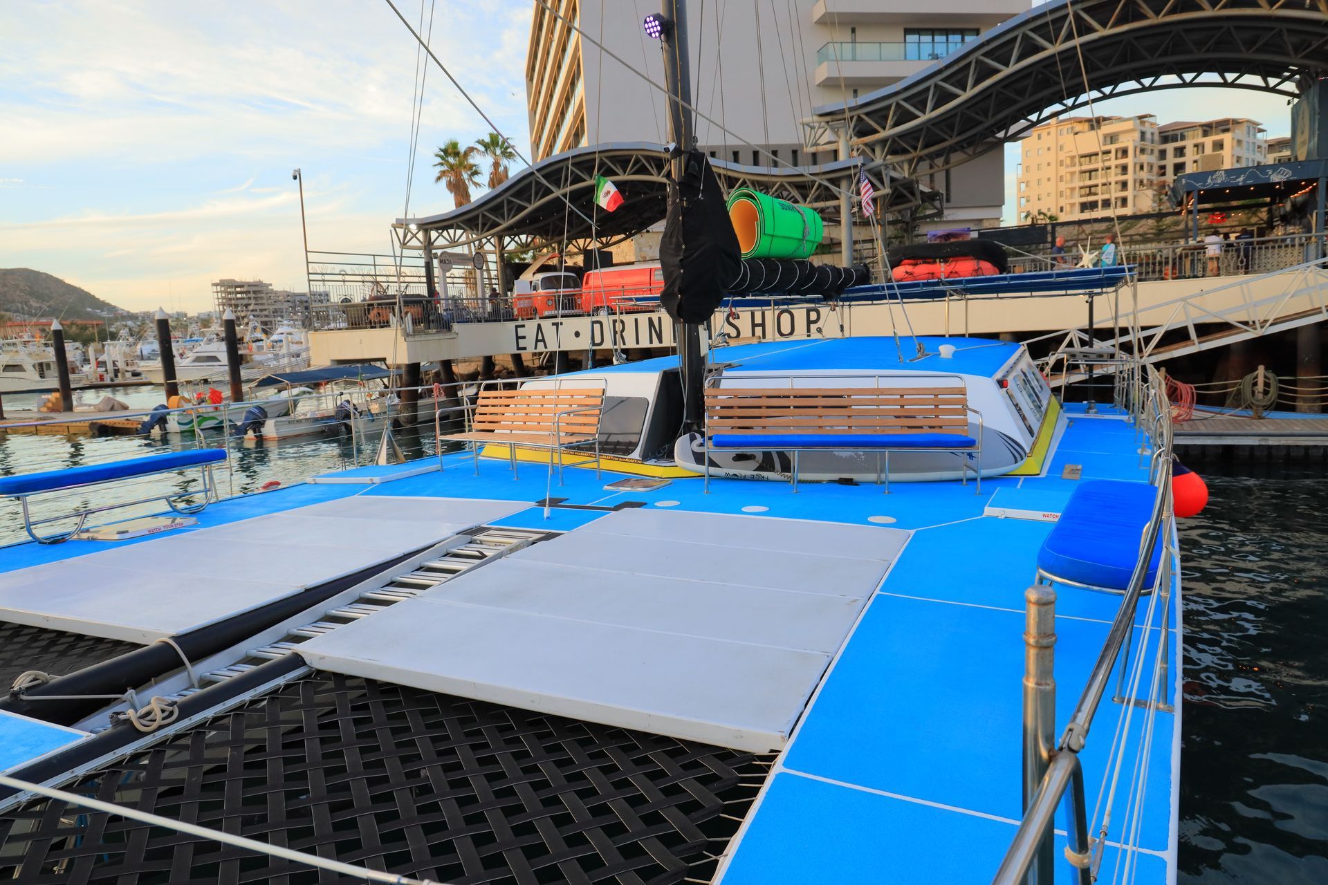 Blue floating dock ramp at a marina beside boats and a city waterfront.
