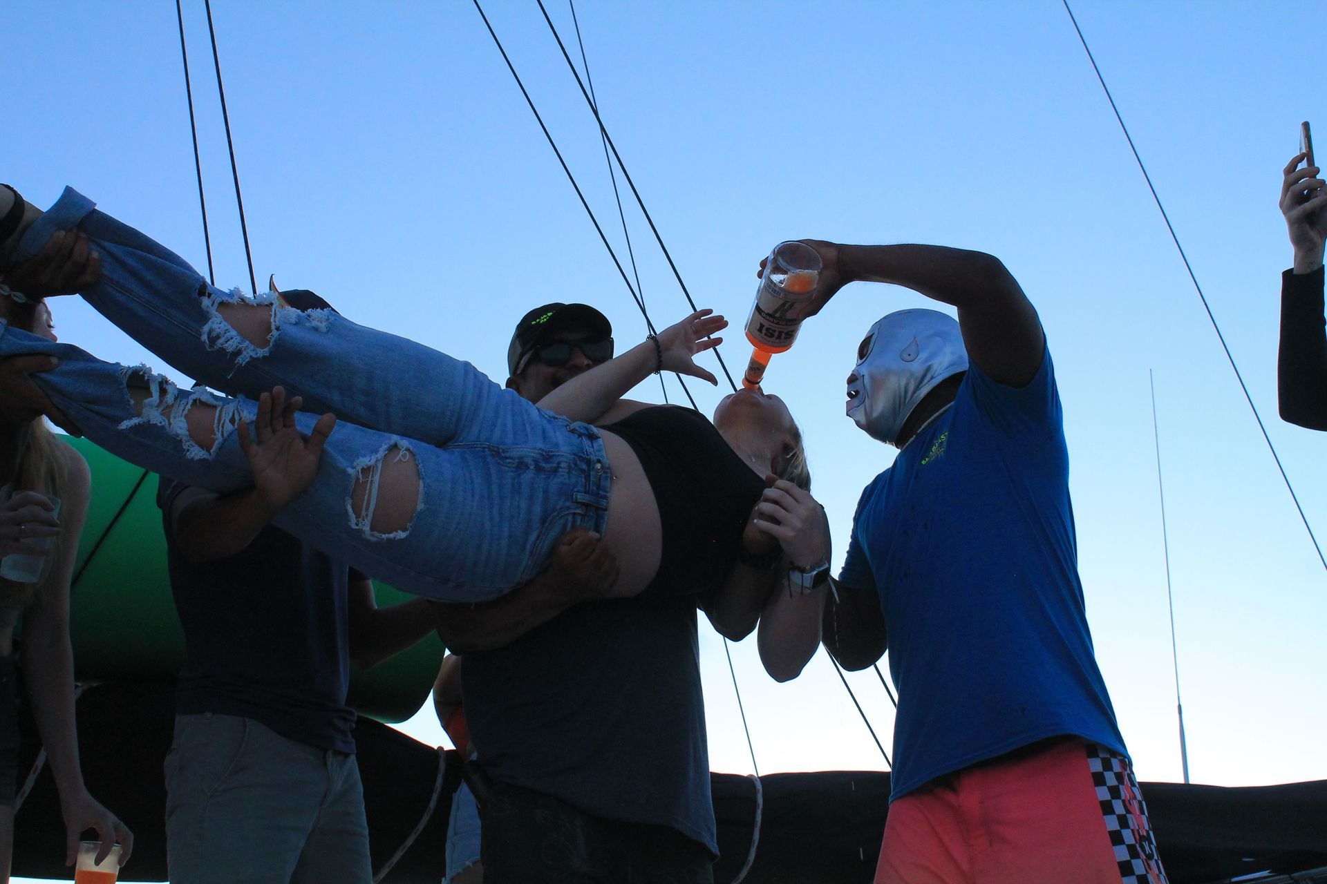 People carrying a person horizontally at dusk, with ropes overhead against the sky.