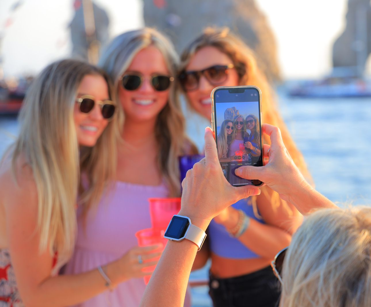 Three friends smile on a boat while someone takes their photo with a smartphone