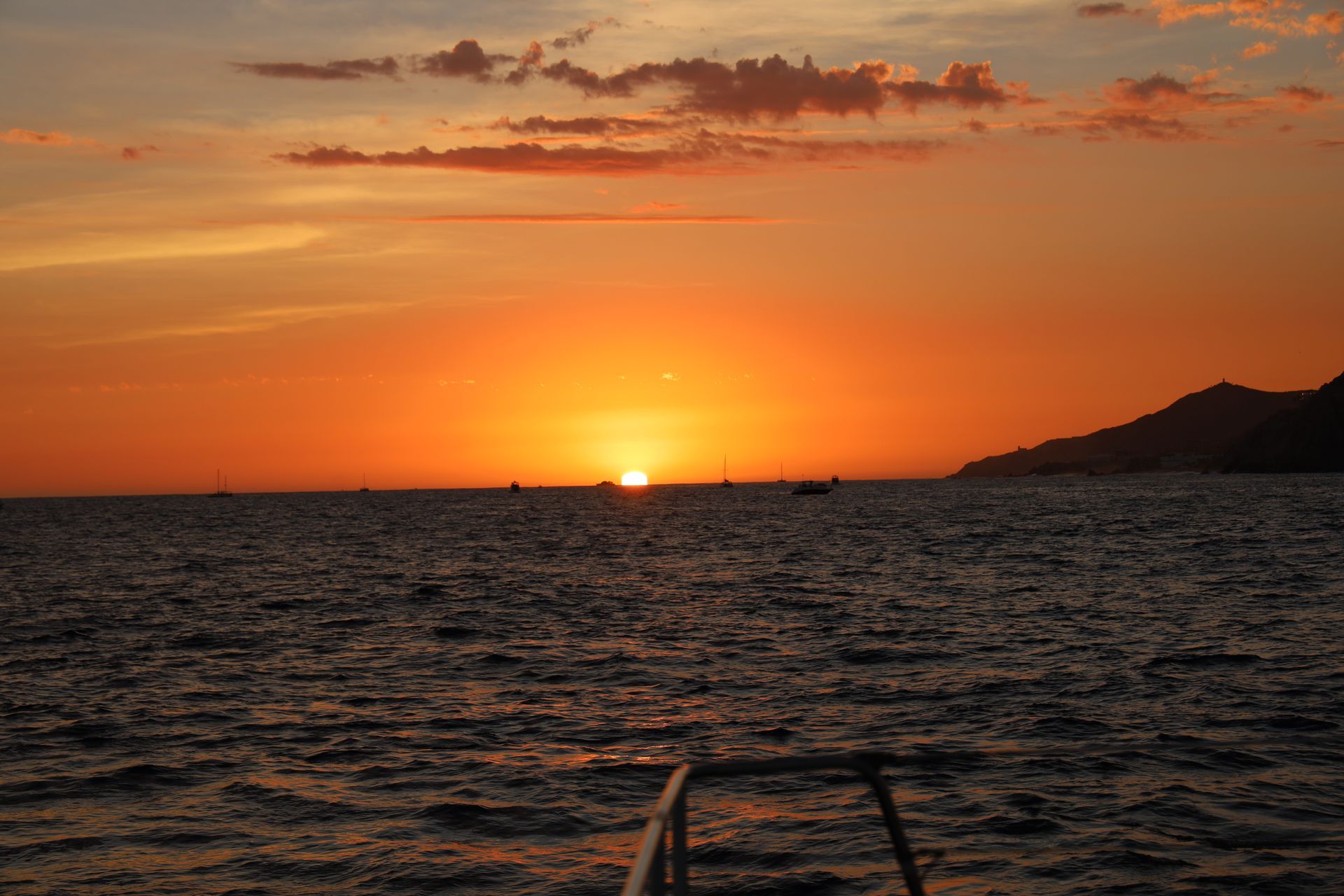 Sunset over calm ocean with orange sky and distant shoreline silhouettes