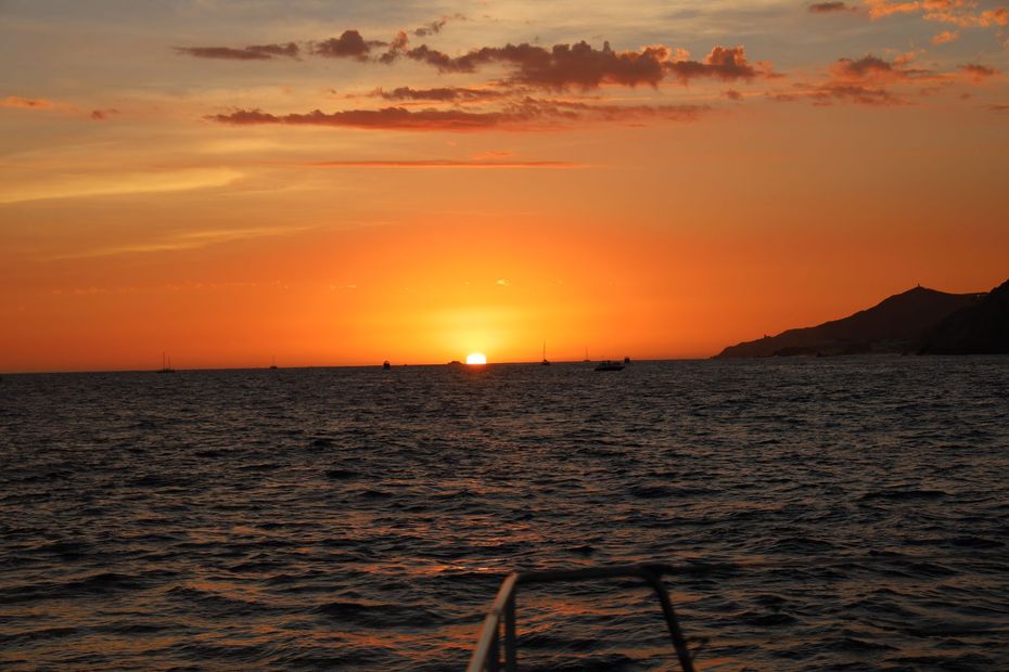 Sunset over the ocean with orange sky, dark waves, and a distant shoreline on the right