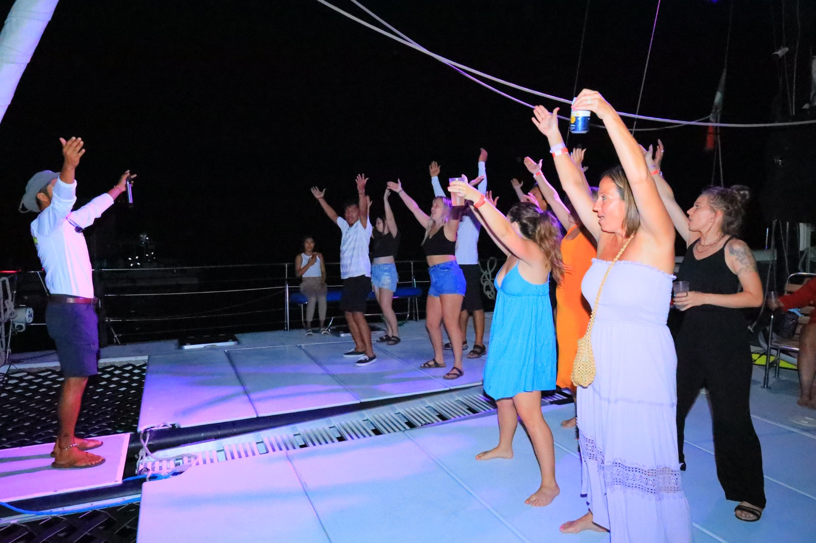 People dancing outdoors at night under string lights, with arms raised on a lit deck.