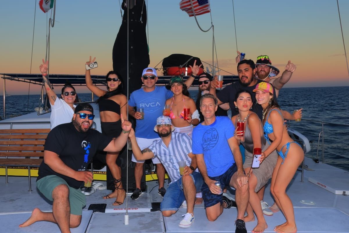 Group of friends posing on a boat at sunset, with ocean and American flags in the background.