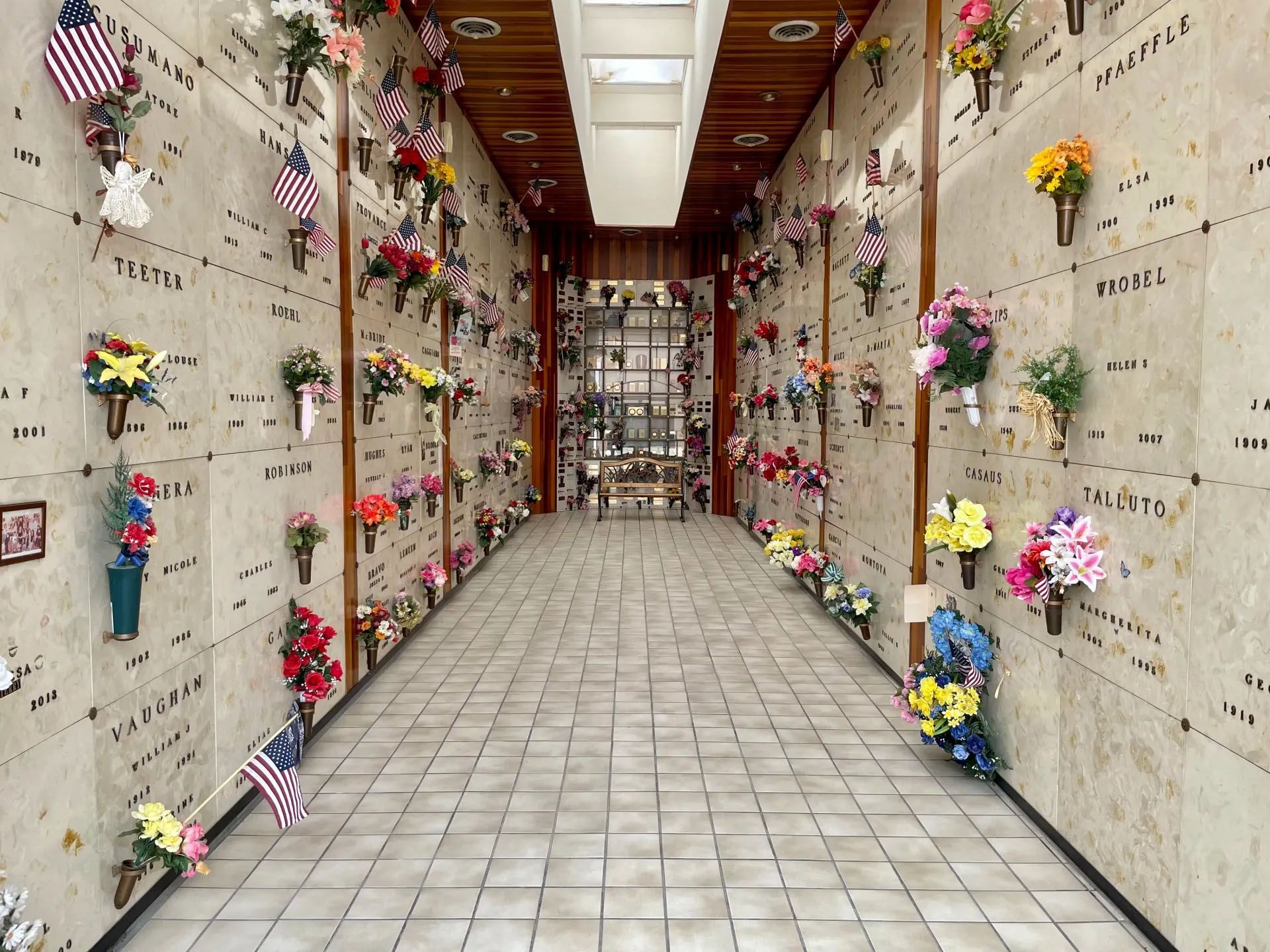 Indoor mausoleum hallway with flowers and American flags in niches.