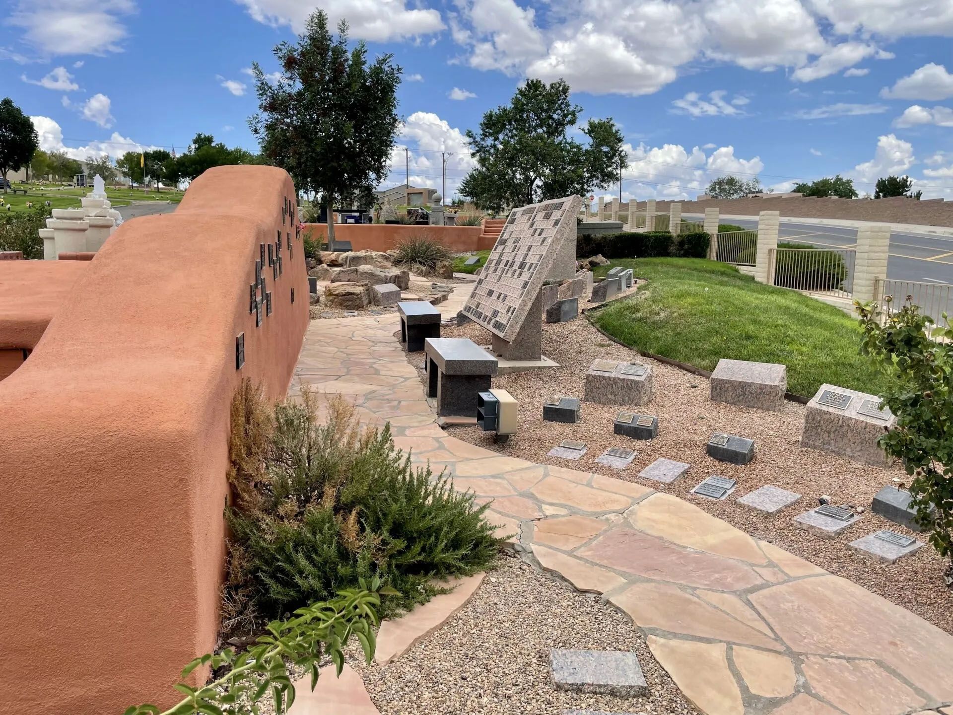 A southwestern-style memorial garden with a stone path, benches, and a large stone sculpture under a blue sky.