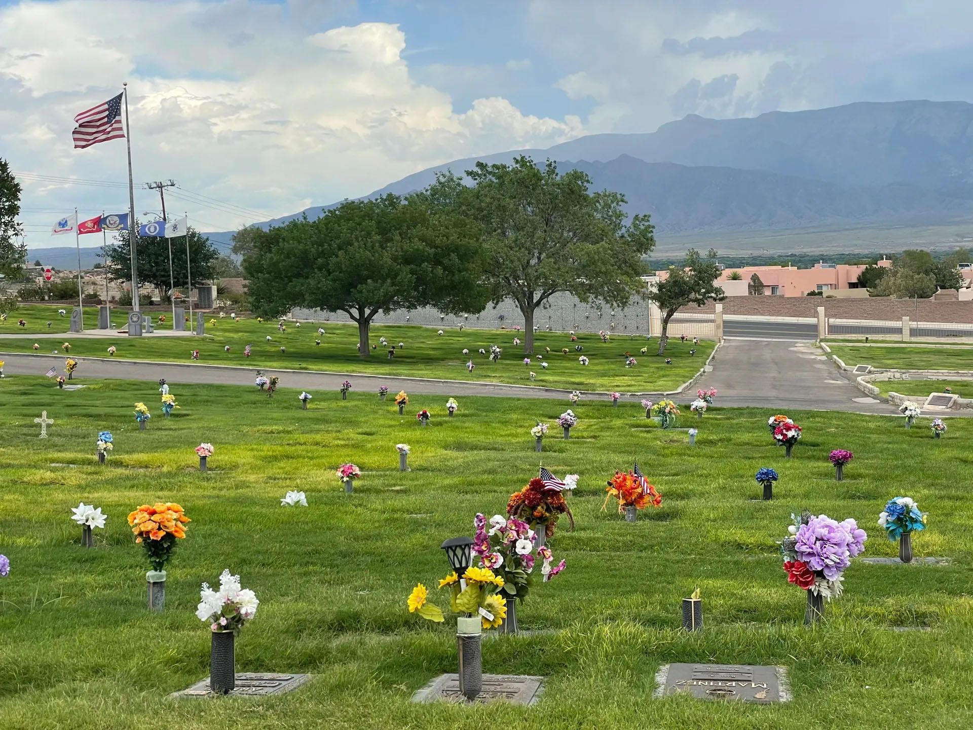 Cemetery with green grass, colorful flowers, and American flag; mountains in the background.