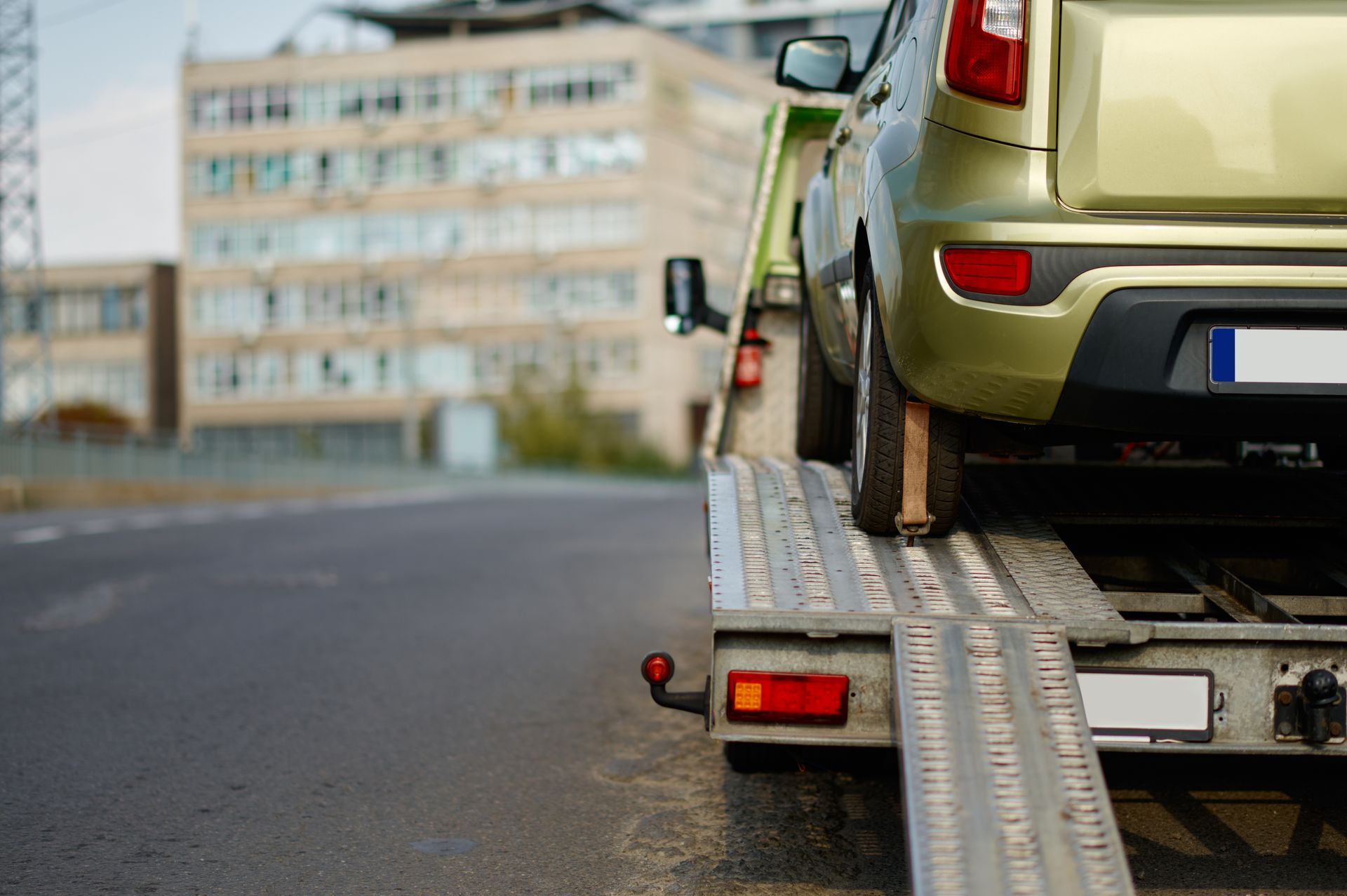 Car loaded onto a flatbed tow truck's ramp on a city street.
