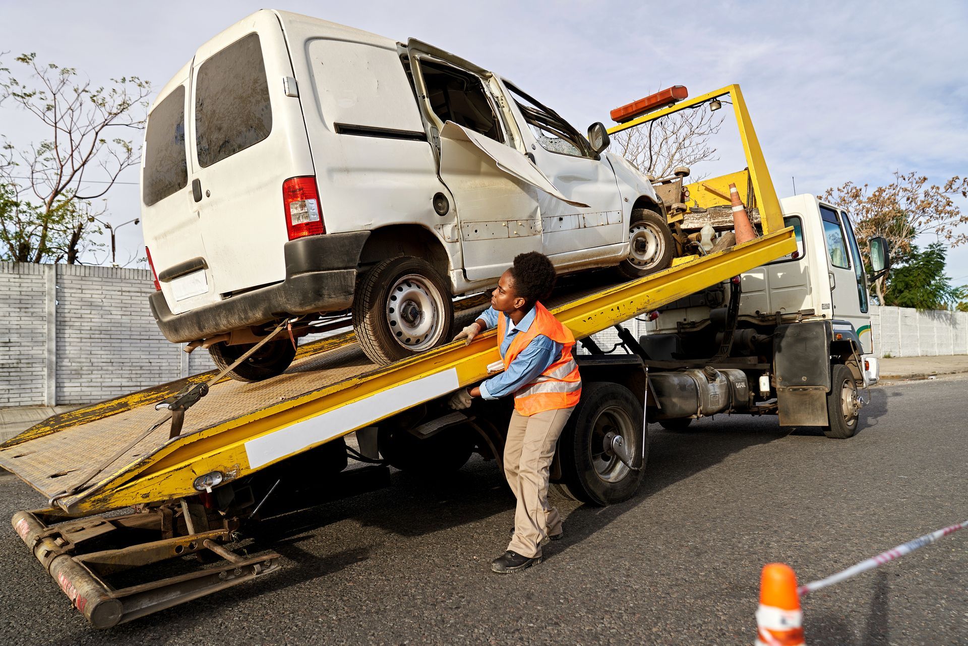 Woman in reflective vest adjusting van on hydraulic platform before removing from crash site.