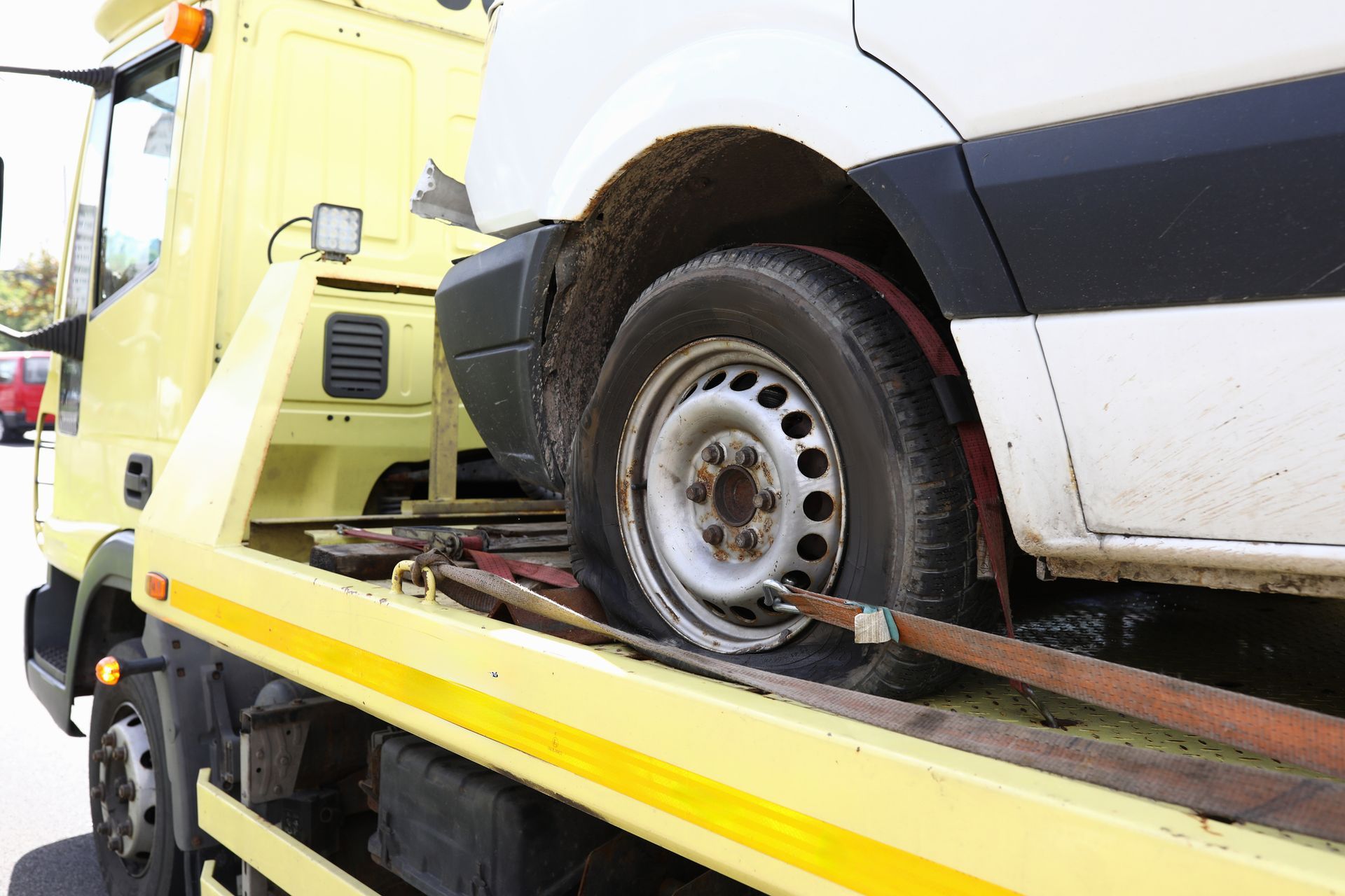 A yellow tow truck carries a damaged white van on its flatbed.