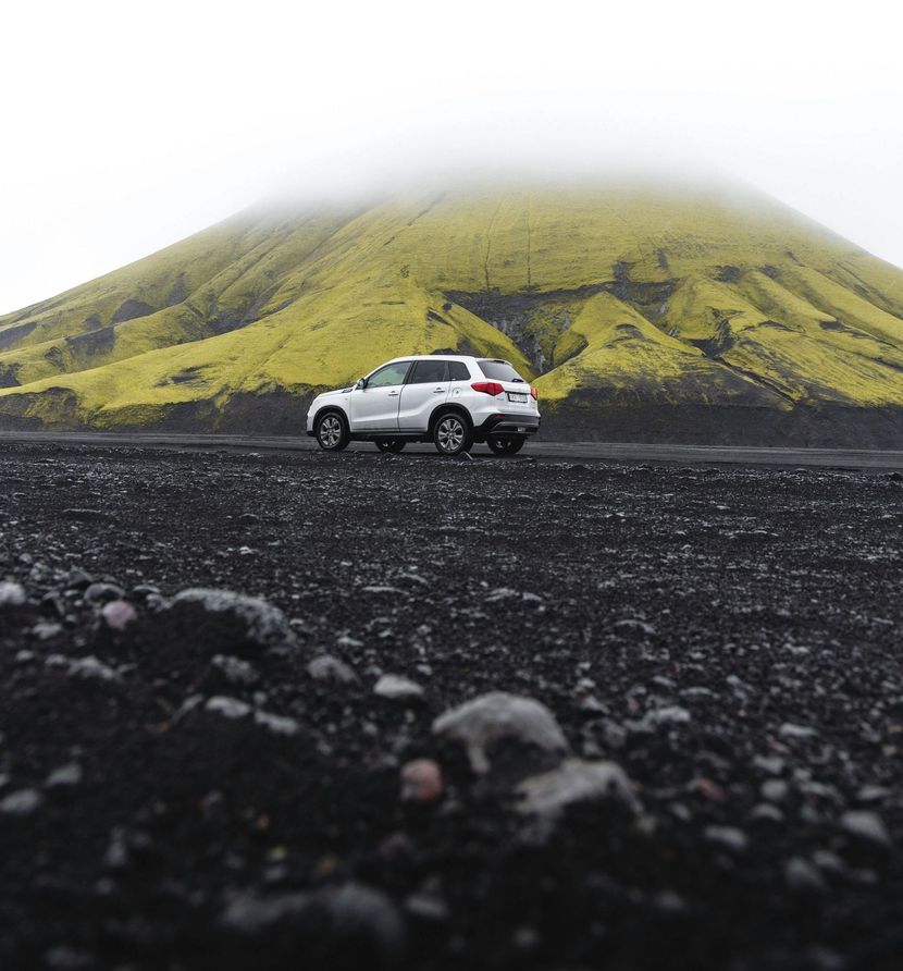 A car is driving down a dirt road in front of a mountain.