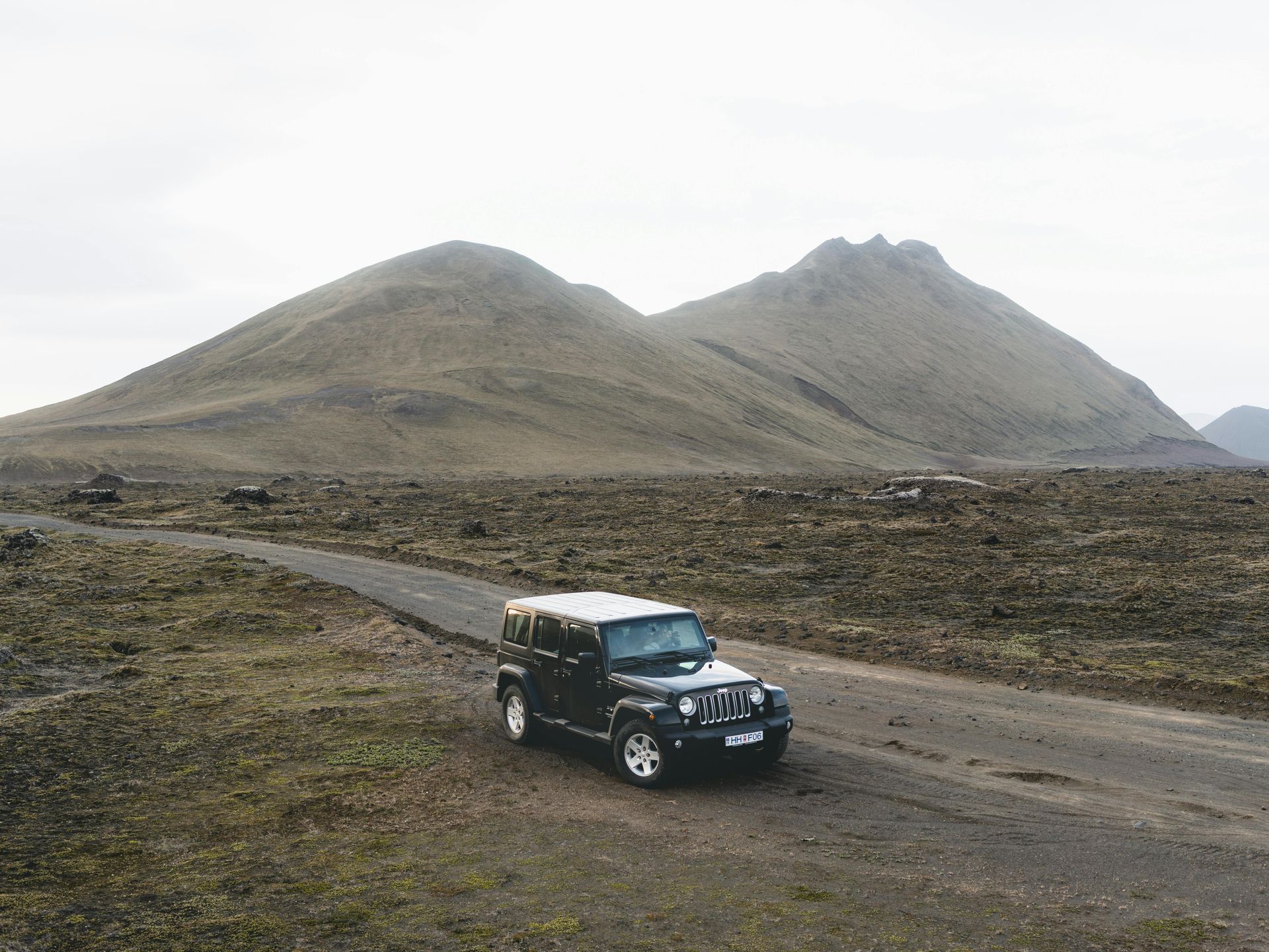 A black jeep is driving down a dirt road in the desert.