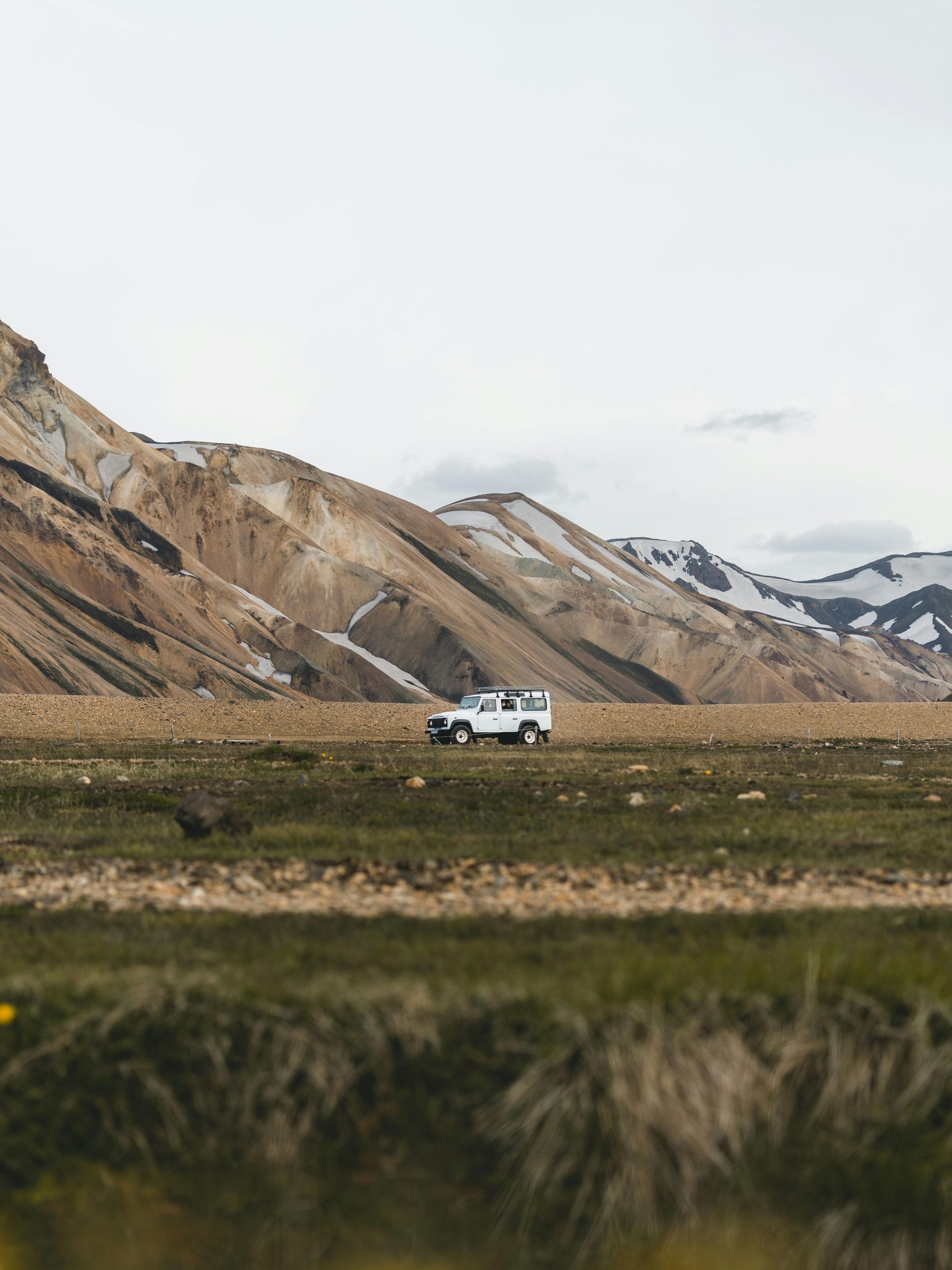 A white truck is driving through a grassy field with mountains in the background.