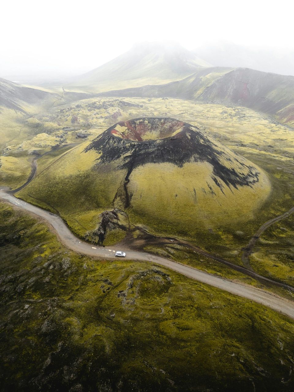 An aerial view of a car driving down a road in front of a volcano.