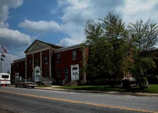 Red brick civic building with white columns beside a road under a cloudy sky