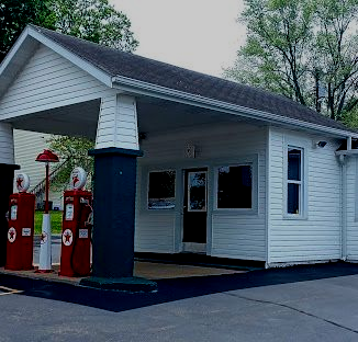 Small white gas station building with red pumps under a sloped roof at dusk
