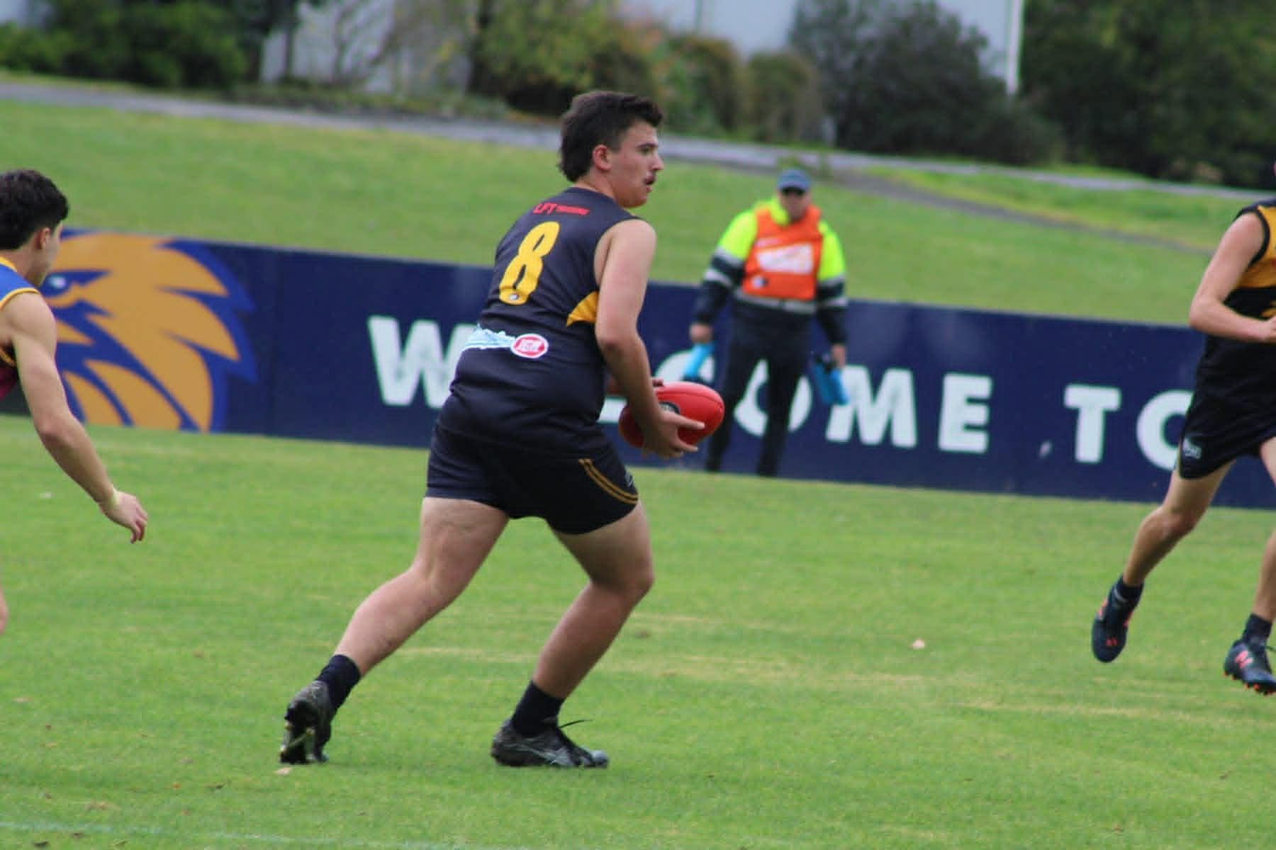Rugby player in black runs with the ball on a grassy field during a match