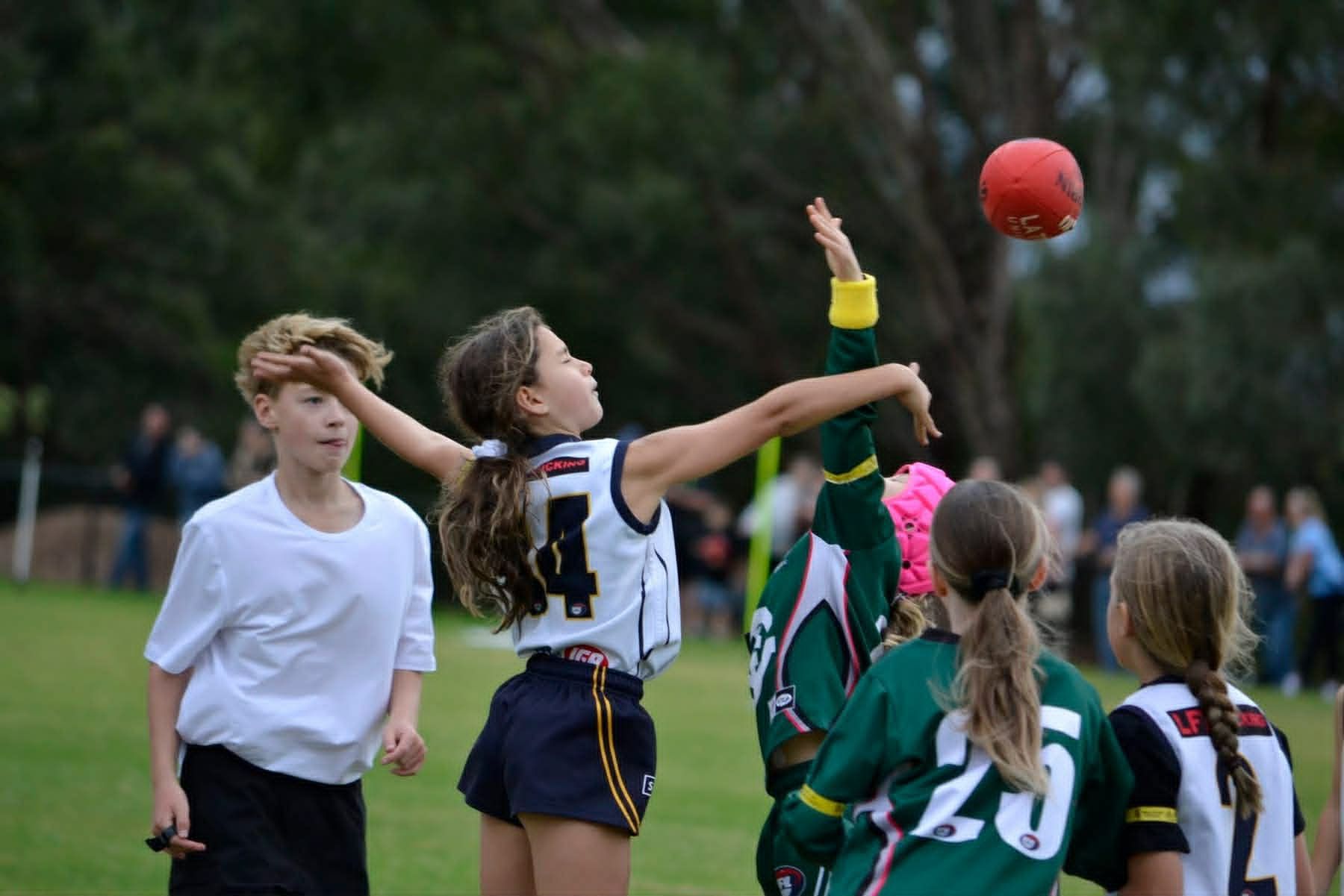 Players reaching for a red ball during a field game outdoors
