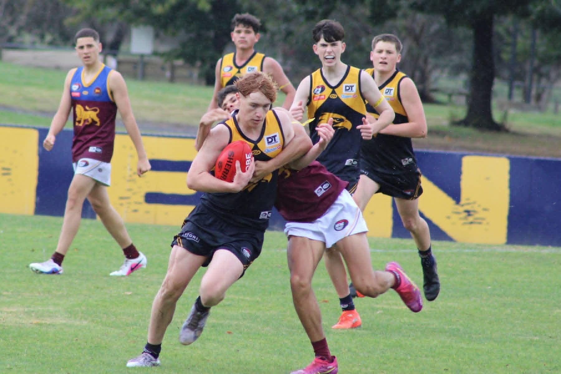 Two players grapple for the ball on a grassy field during an Australian rules football game.