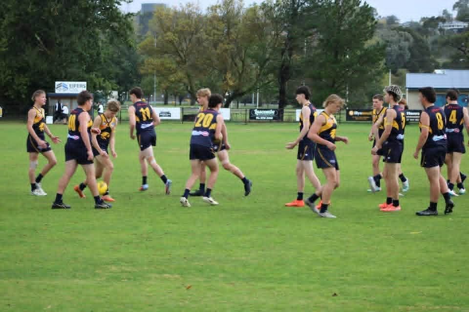A group of athletes in black and yellow uniforms standing on a grassy field during a sports game.