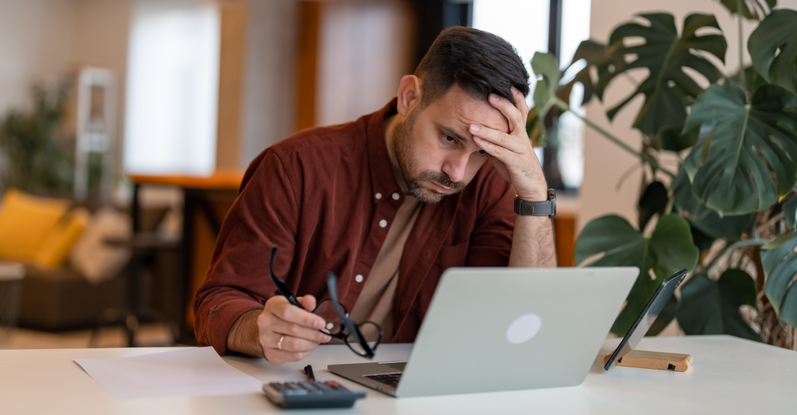 A frustrated man is sitting at a table looking at a laptop computer.