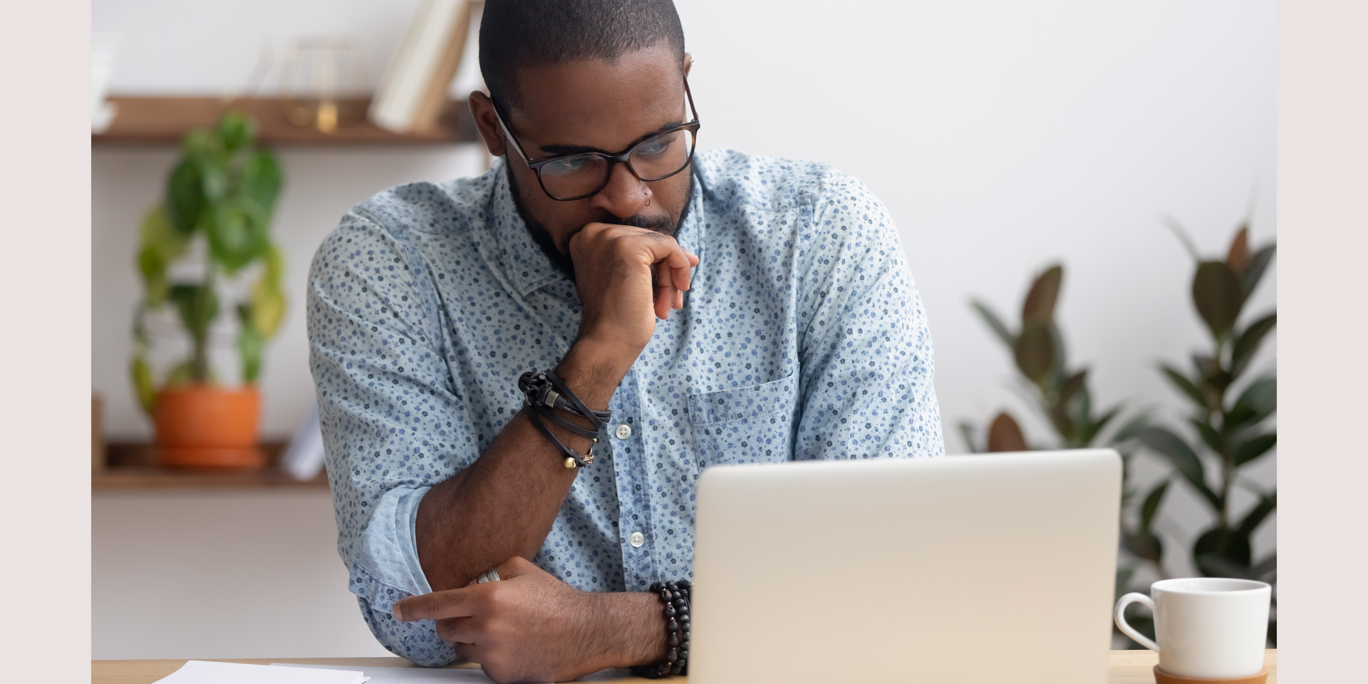 A man with his hands on his face is looking worried at a laptop.