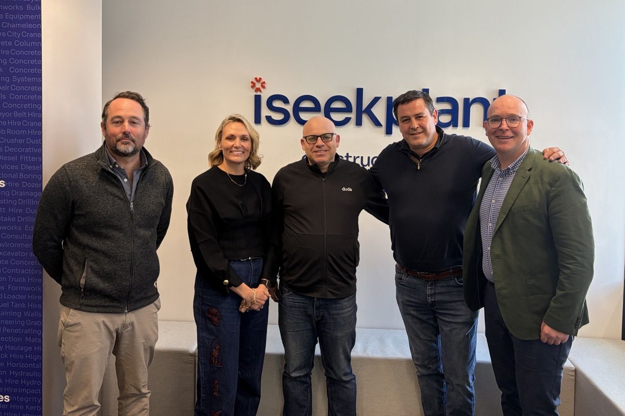 Five people stand smiling in front of an iseekplant wall logo.
