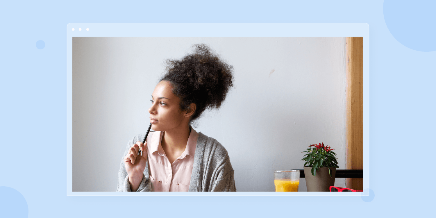 A woman is sitting at a table with a pencil in her mouth
