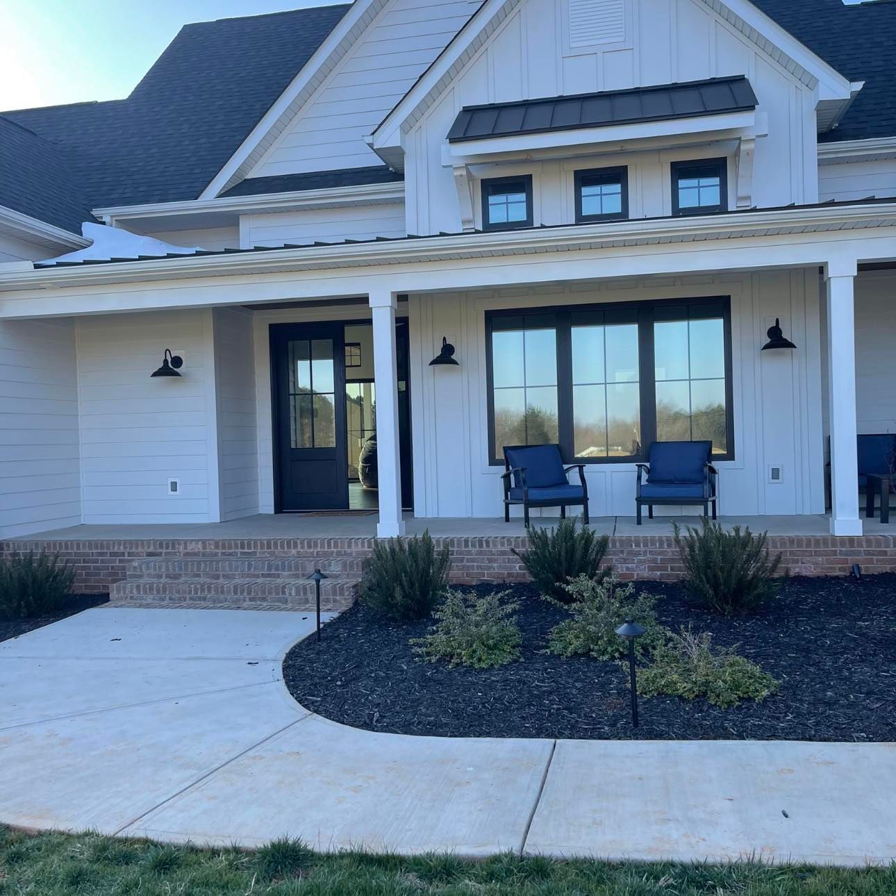 White farmhouse with a porch, black accents, and blue chairs.