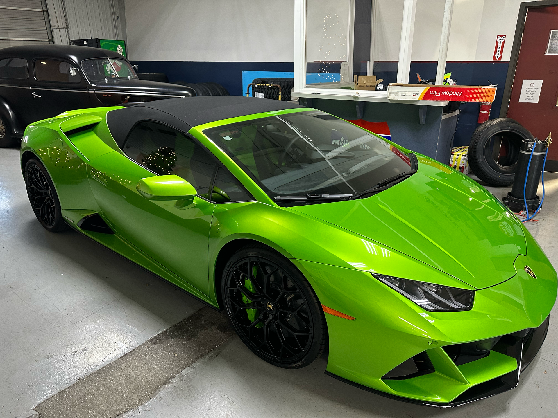 Bright green Lamborghini convertible with black roof and wheels in a garage.