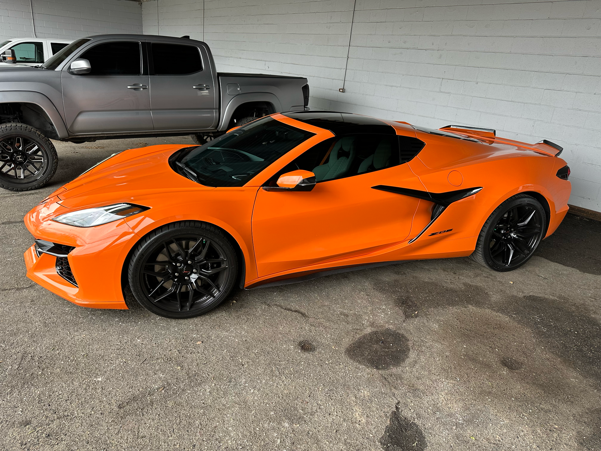 Orange sports car with black accents parked next to a silver truck in a garage.
