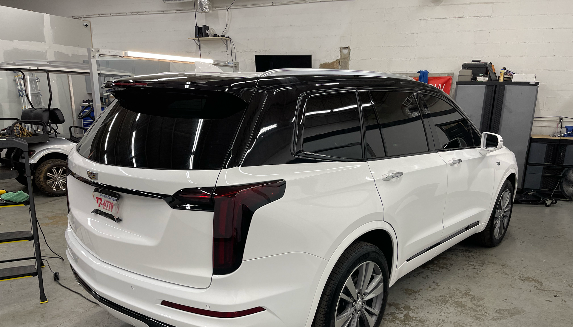 White Cadillac SUV with black roof and tinted windows inside a garage.