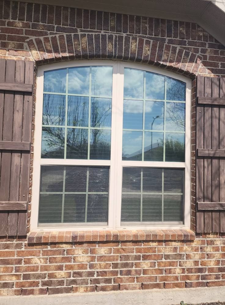 Window with white frame and arched top, surrounded by brick. Brown shutters on either side.