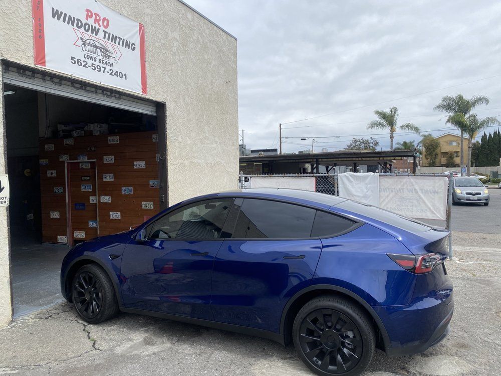 Blue Tesla Model Y parked outside a window tinting shop with tinted windows.