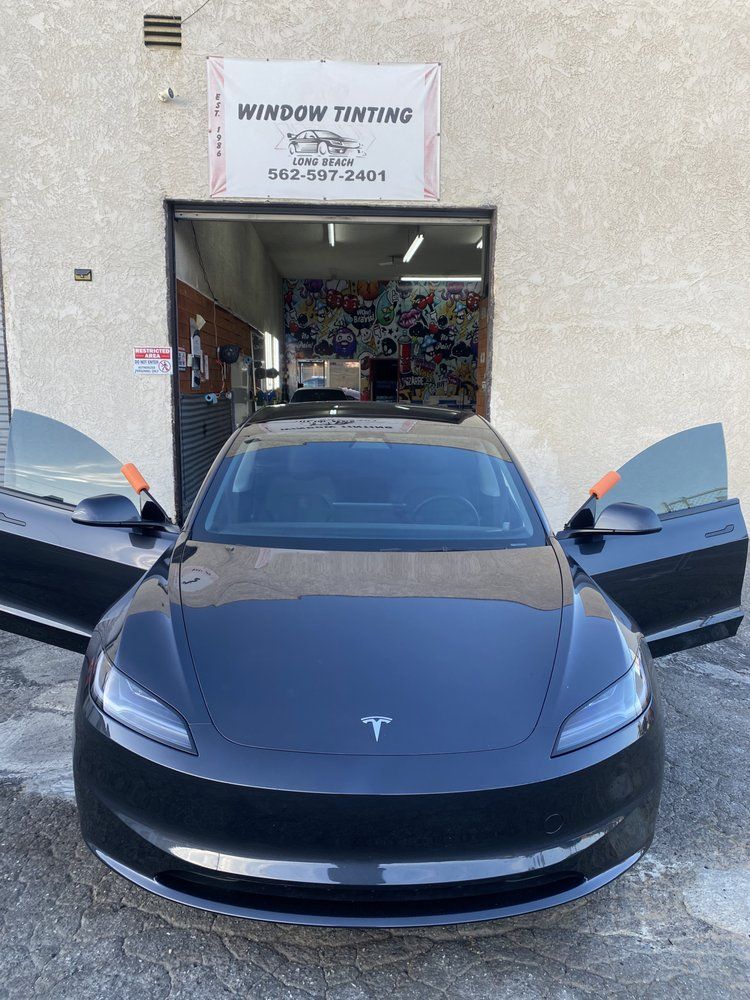 Black Tesla with tinted windows, parked in front of a window tinting shop with open doors.