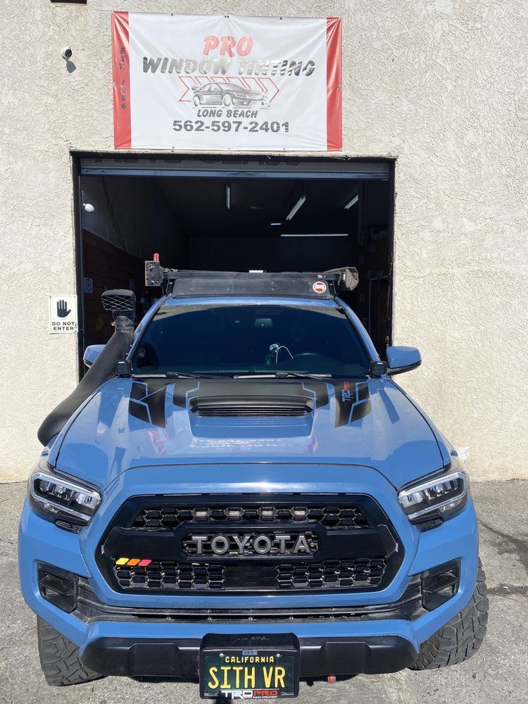 Blue Toyota Tacoma truck with modifications in front of a shop.