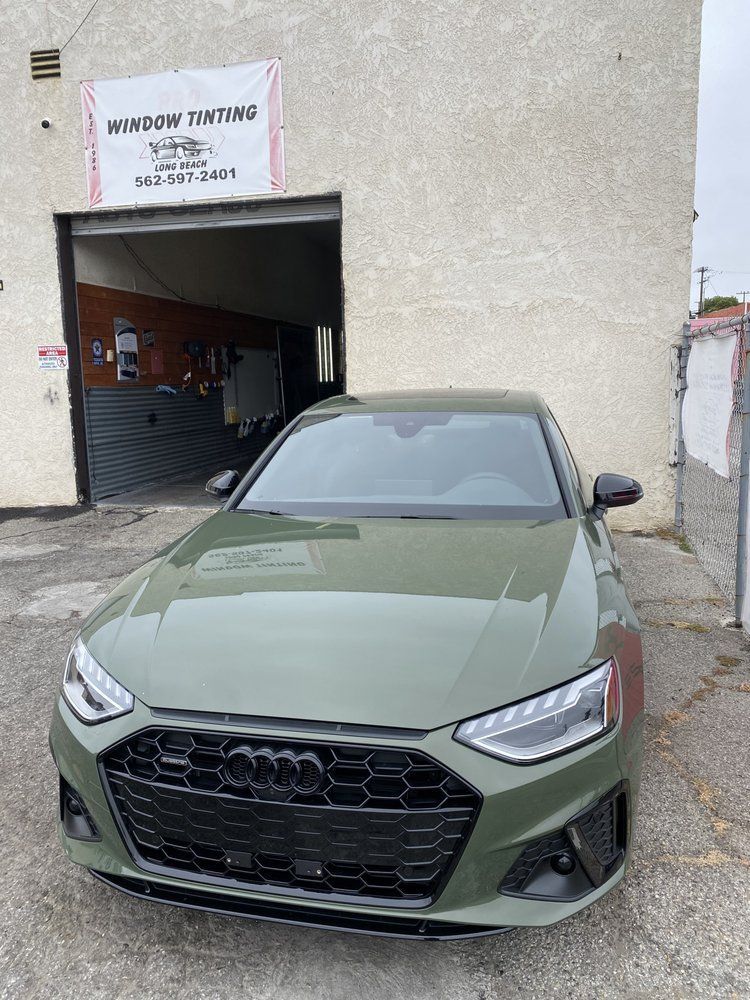Green Audi sedan parked in front of a window tinting shop with a black grille and tinted windows.