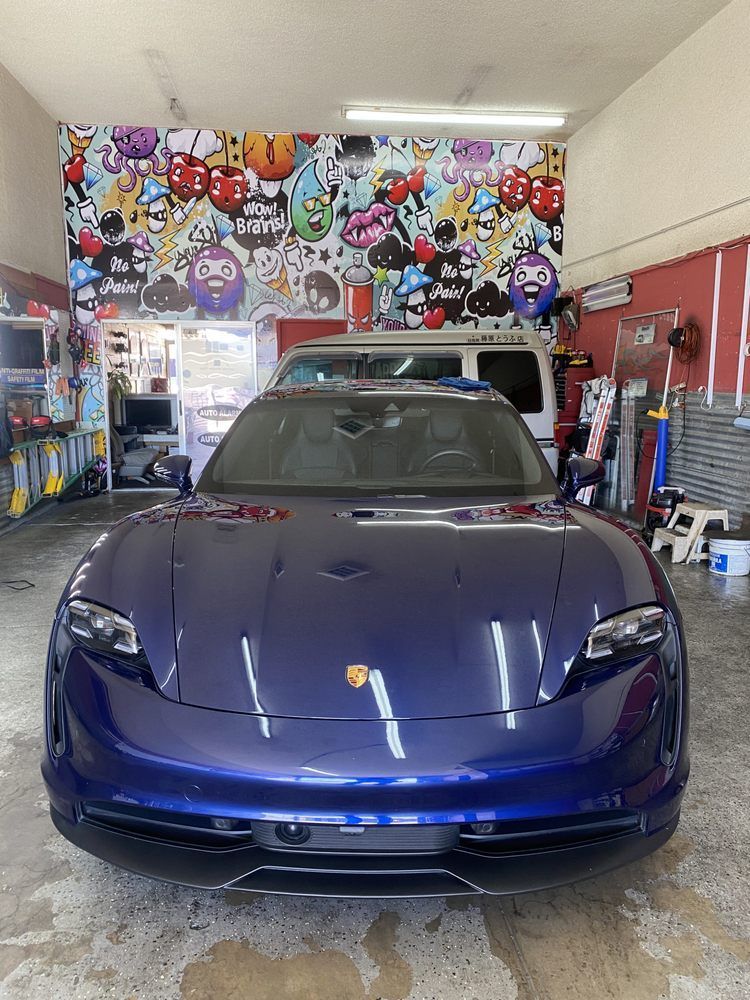 Blue Porsche electric car parked inside a garage with a graffiti wall.