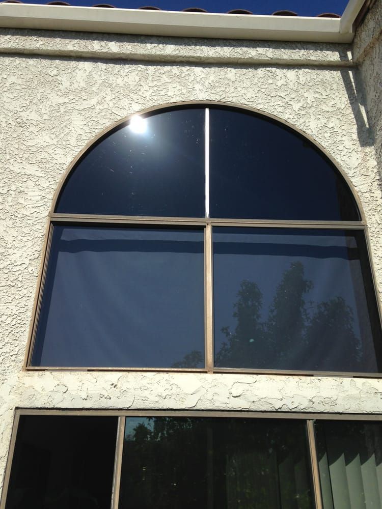Large arched window with tinted glass on stucco building, reflecting sky and sun.