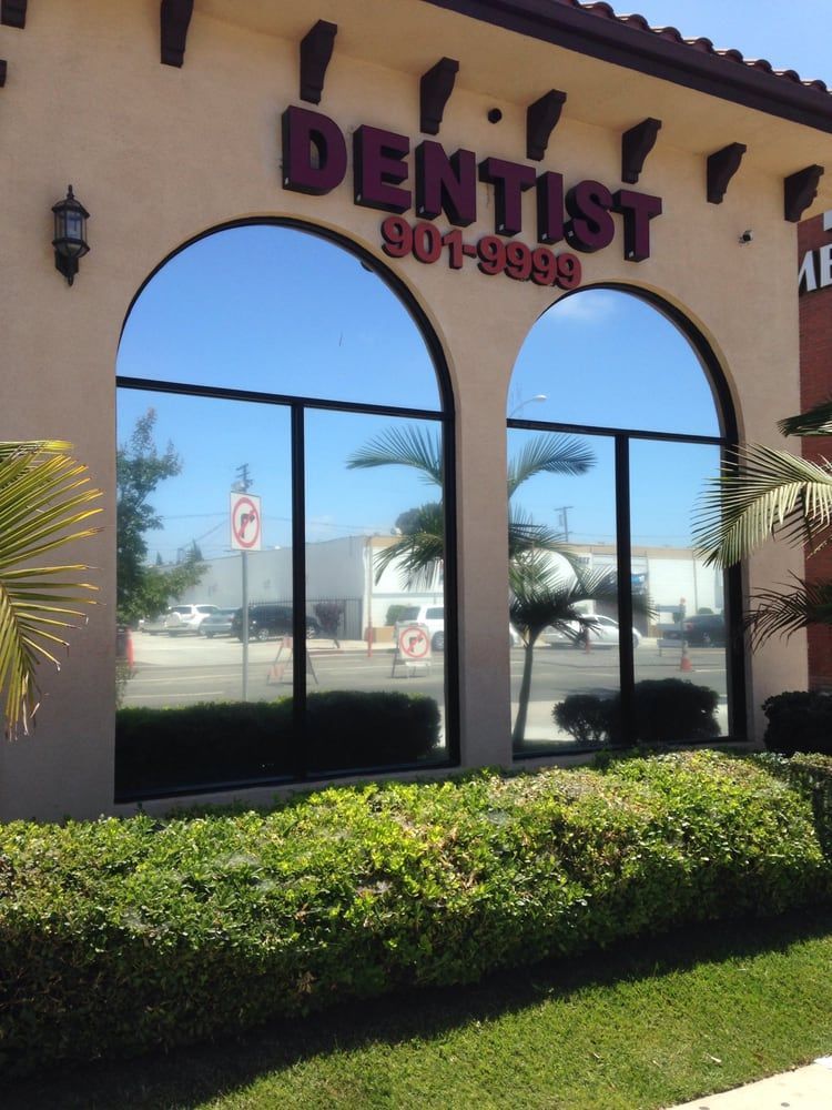 Dentist office exterior with large arched windows, reflective glass, and a green hedge.