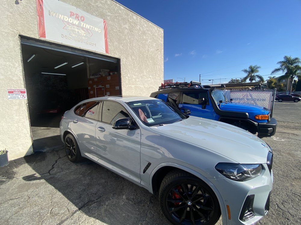 Gray BMW SUV parked outside a business with a blue truck behind it. Sign above reads 
