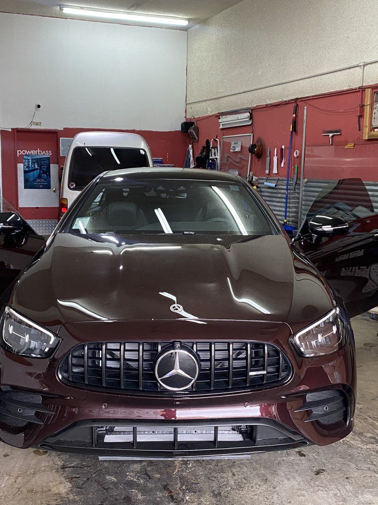A maroon Mercedes-Benz with black grille inside a garage, doors open.