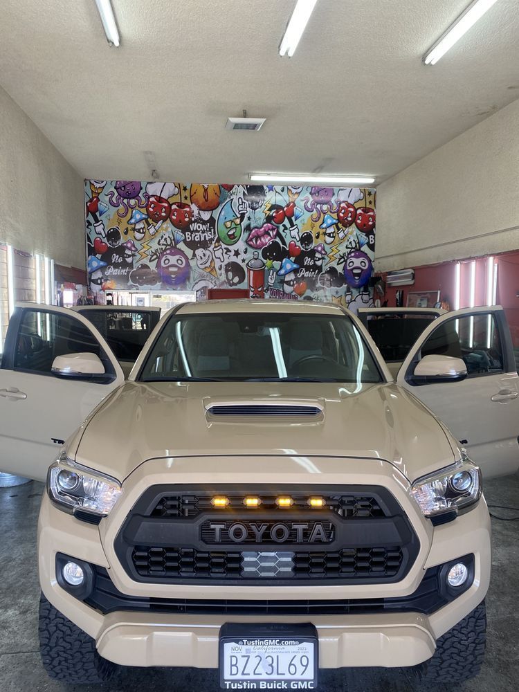 Tan Toyota Tacoma truck with doors open, in front of a graffiti wall.
