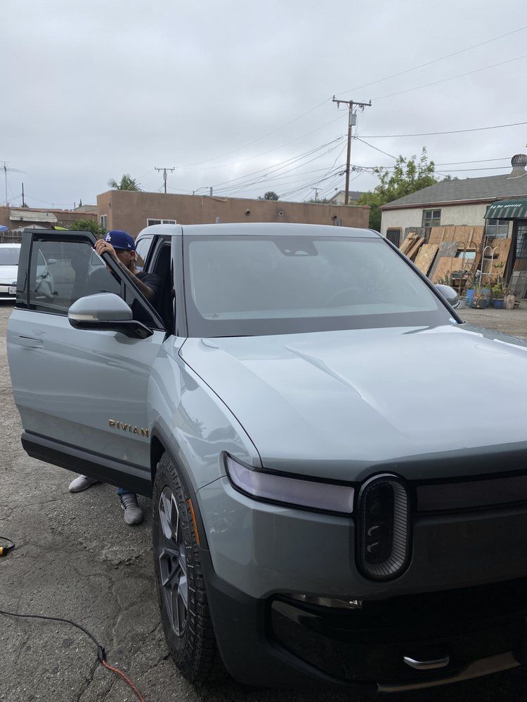 Gray Rivian electric truck; a person opens the driver's side door. Cloudy day outside a building.