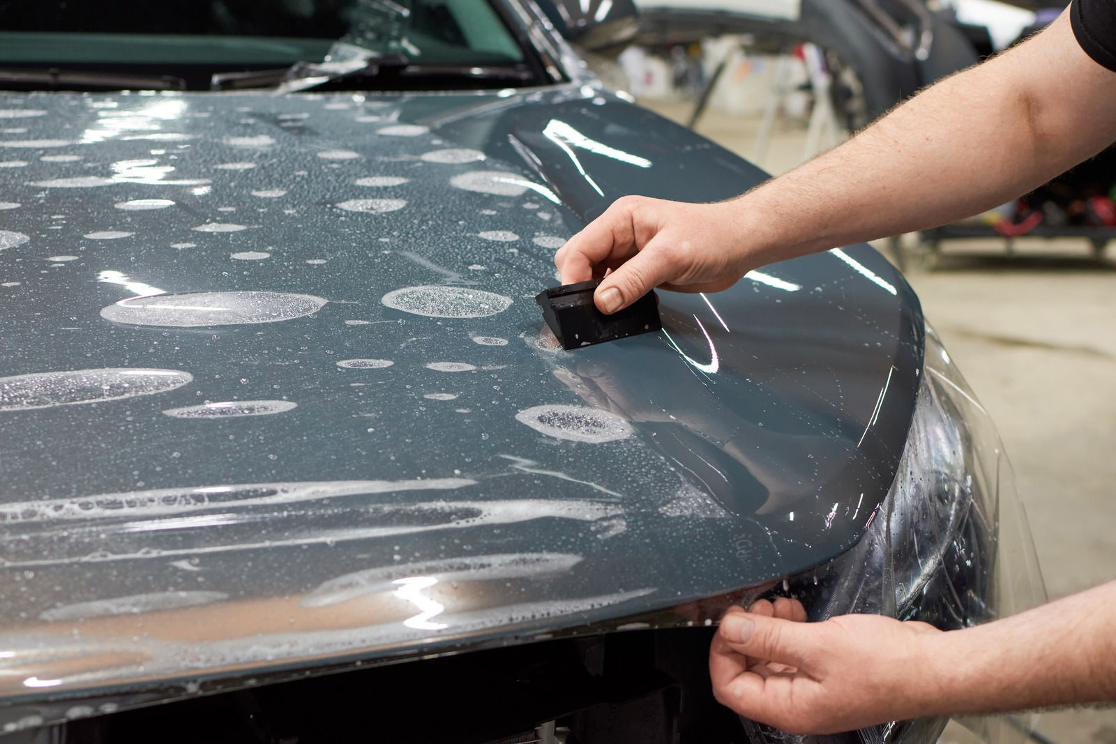 Person applying clear protective film to a car hood using a squeegee.