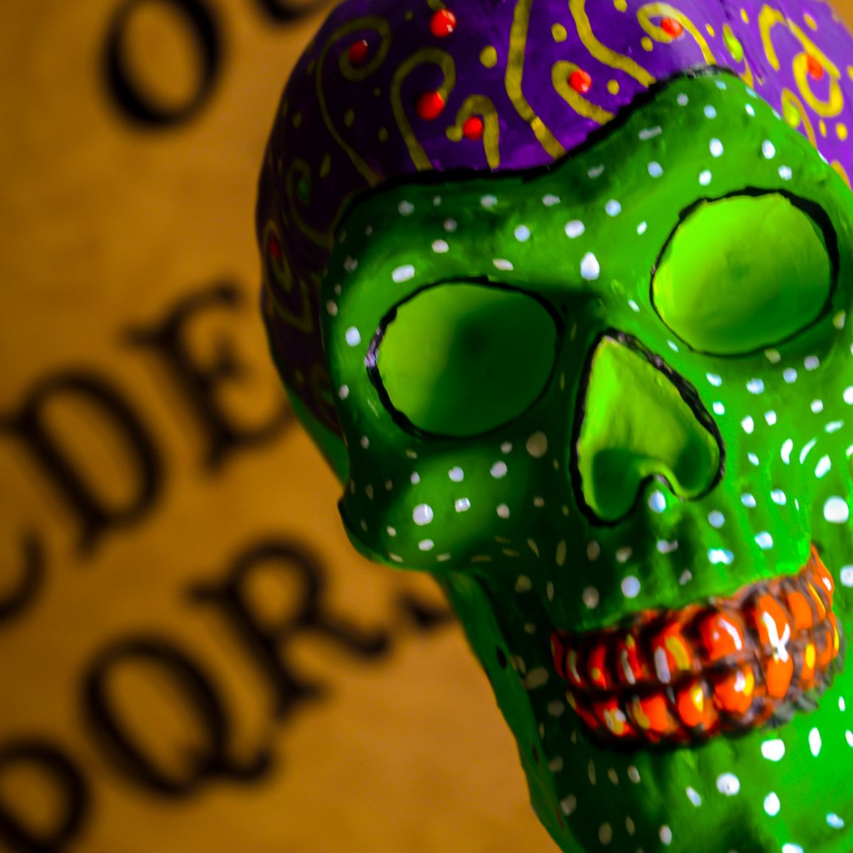 A green skull with a purple hat is standing in front of the alphabet