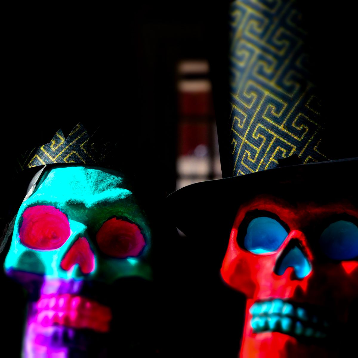 Two colorful skulls wearing top hats in a dark room