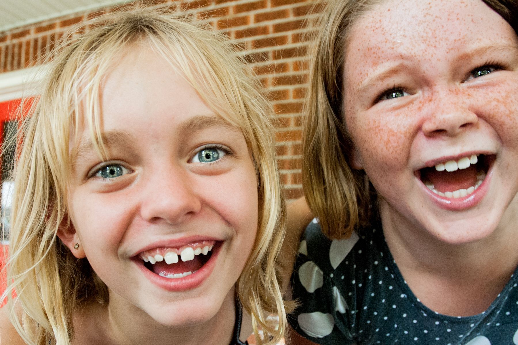 Two young girls are laughing together in front of a brick building.