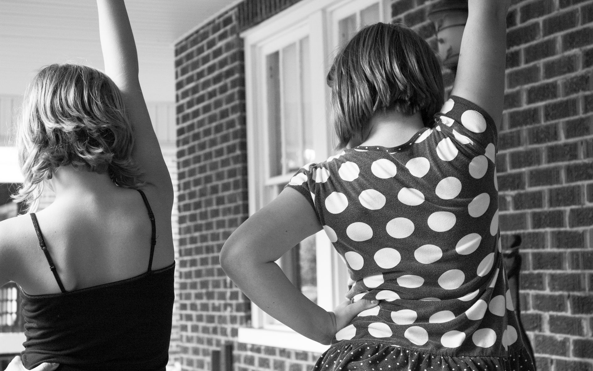 Two women are standing in front of a brick wall with their arms in the air.