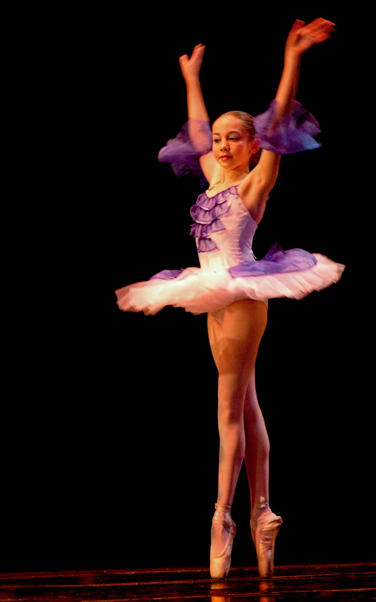 The ballerina is wearing a purple tutu and pointe shoes